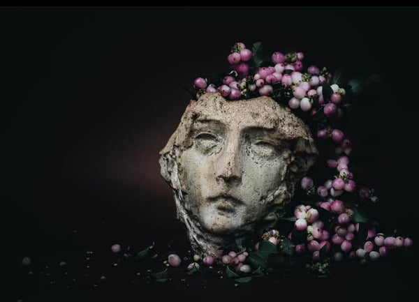 photograph of stone face with purple foliage and berries as hair